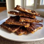 A stack of broken pieces of rich graham cracker toffee with a dark chocolate topping on a white plate.