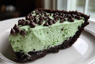 A close-up slice of bright green grasshopper pie with a dark chocolate crust, topped with mini chocolate chips.
