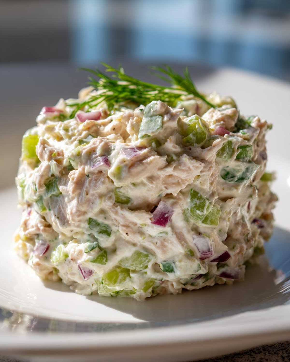 A perfectly molded portion of healthy tuna salad featuring tuna, celery, and red onion in a creamy dressing, garnished with dill.