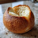 A freshly baked, hollowed-out bread bowl with a golden-brown, textured crust, ready for soup.