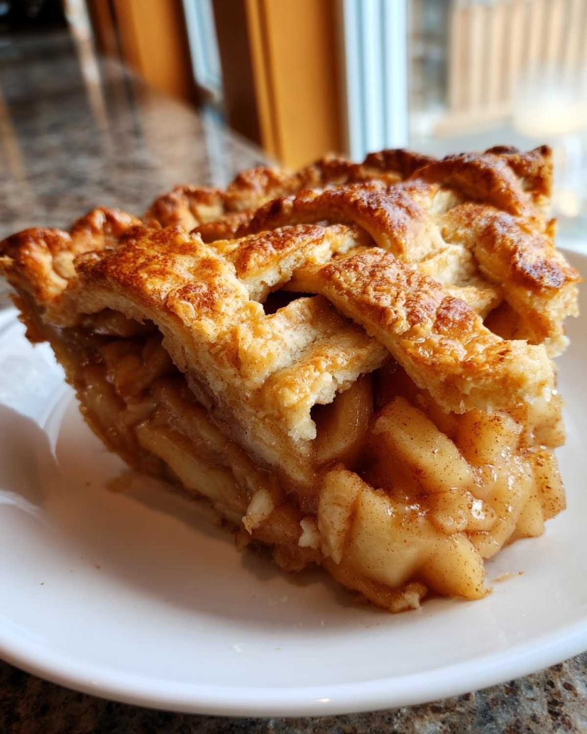 Close-up of a thick slice of homemade apple pie featuring a golden lattice crust and cinnamon-spiced apple filling.