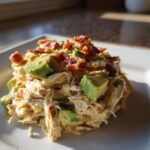 A mound of creamy honey mustard chicken salad topped with diced avocado and crispy bacon bits on a white plate.