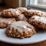 A stack of freshly baked iced oatmeal cookies with a thick white glaze on a white plate.