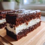 Close-up of a slice of Italian love cake featuring dark chocolate cake layers and a thick white cream filling, topped with glossy chocolate ganache.
