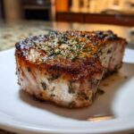Close-up of a thick, juicy air fryer pork chops with a beautiful brown sear and fresh herbs on top.