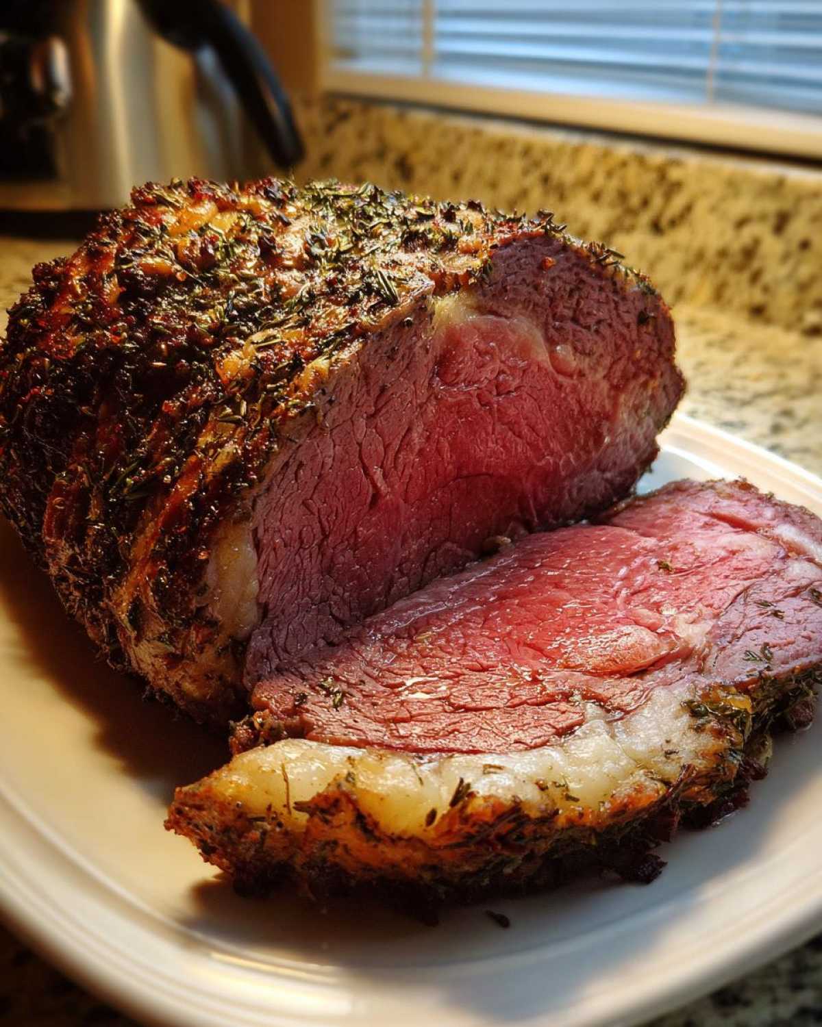 A juicy, medium-rare rib roast, heavily crusted with herbs, has been sliced open on a white plate.