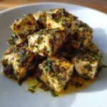 Close-up of cubes of marinated cheese generously coated in green herbs and oil, showcasing the flavor boost.