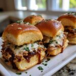 Close-up of gooey melted cheese topping shredded bbq chicken sliders on soft rolls, sprinkled with parsley.