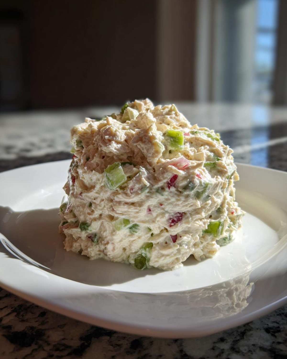 A perfectly molded scoop of creamy healthy tuna salad mixed with celery and red onion on a white plate.