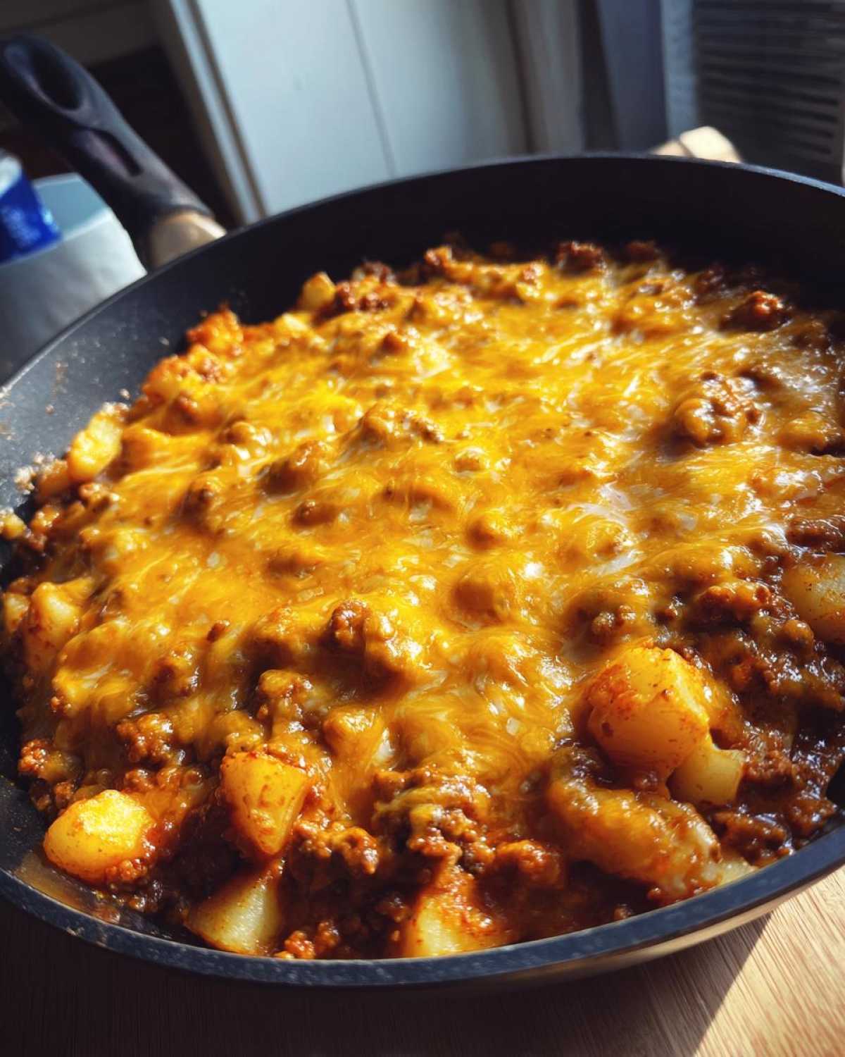 Close-up of Cheesy Taco Potatoes bubbling in a black skillet, topped with melted orange cheddar cheese.