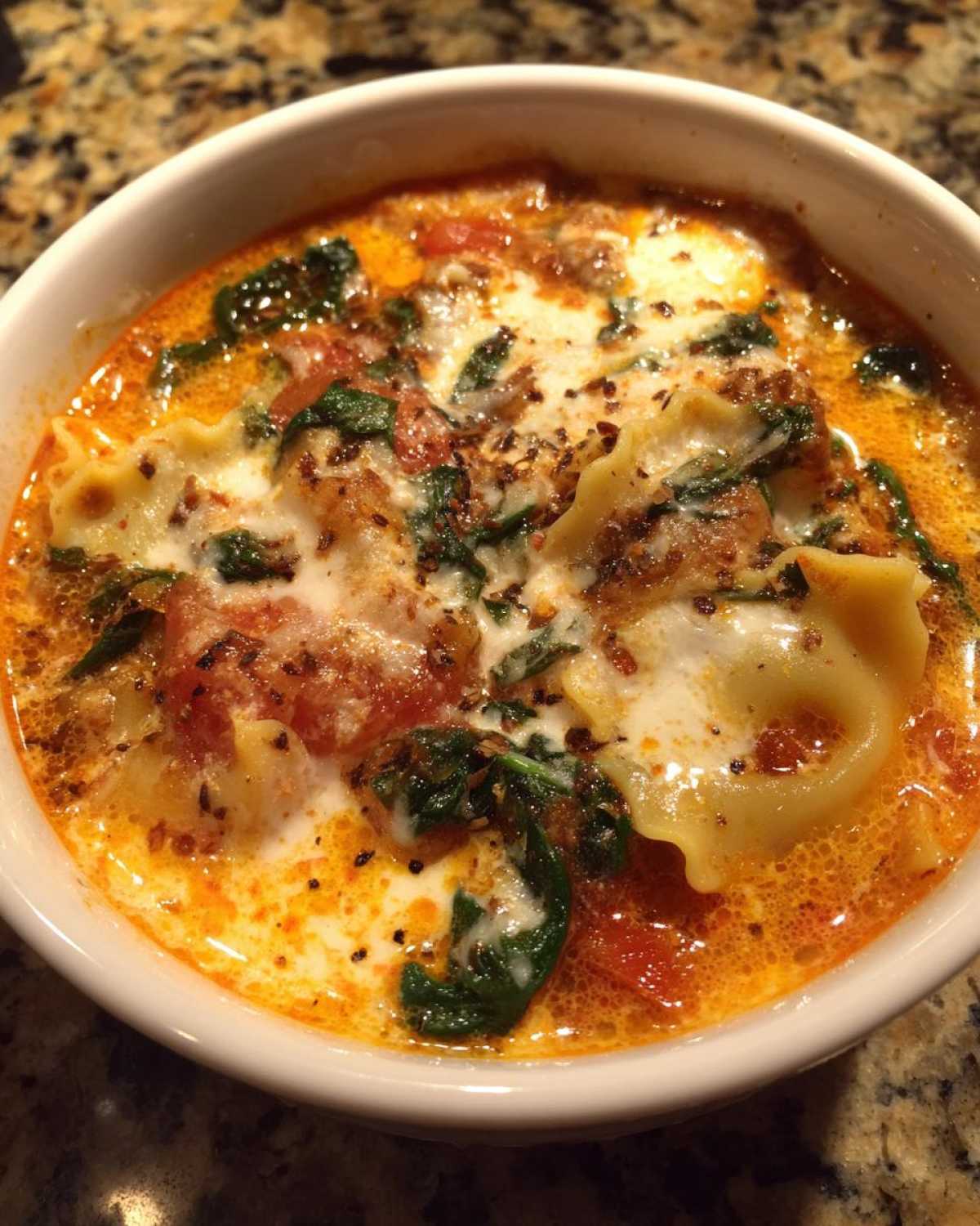 Close-up of a white bowl filled with rich, orange broth, pasta, spinach, and a swirl of cream, representing one pot lasagna soup.