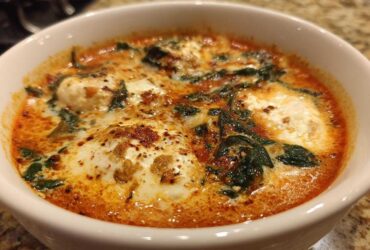 Close-up of a bowl of rich one pot lasagna soup topped with melted ricotta cheese dollops and wilted spinach.