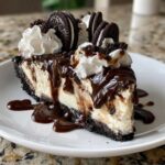 A rich slice of Oreo ice cream pie topped with whipped cream, chocolate fudge, and whole cookies.