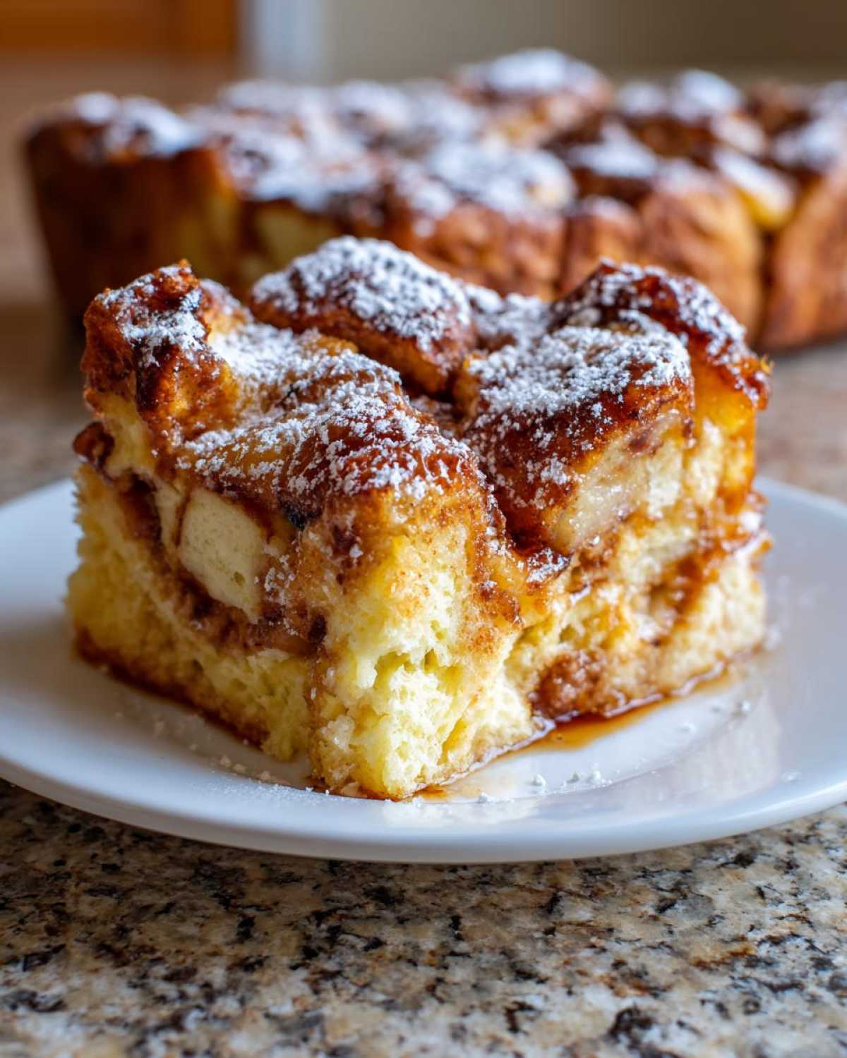 A close-up slice of moist overnight french toast, dusted with powdered sugar, served on a white plate.
