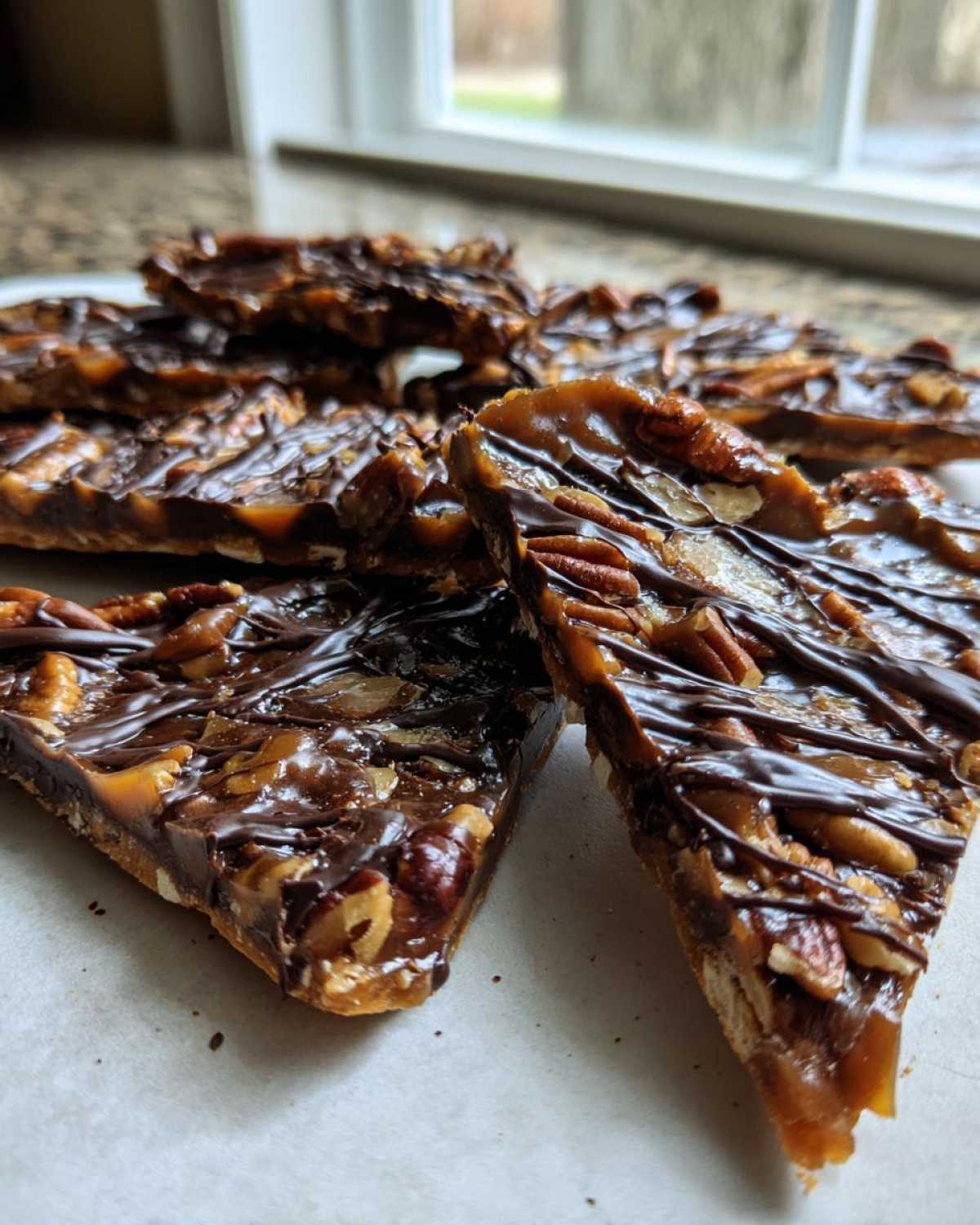 Close-up of several triangular slices of rich Pecan Pie Bark topped with pecans and drizzled chocolate.