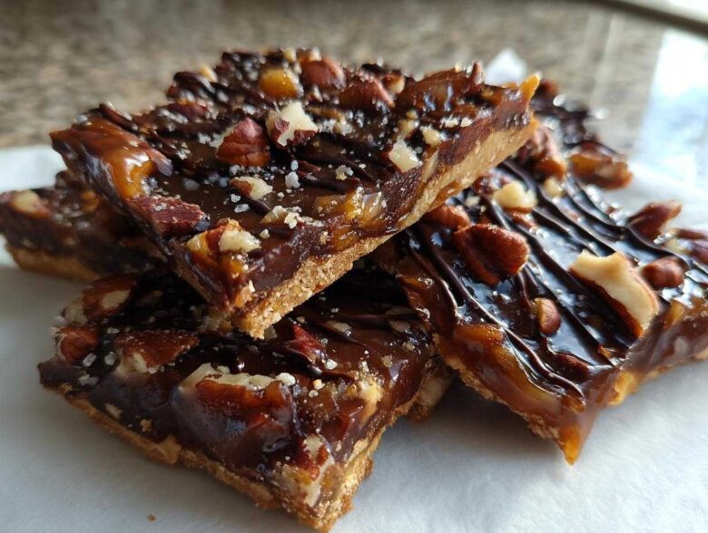 Close-up of stacked slices of rich Pecan Pie Bark with a shortbread crust, caramel, chocolate drizzle, and sea salt.