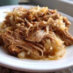 Close-up of tender, shredded pork and sauerkraut served on a white plate, highlighting the moist texture.