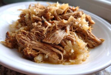 Close-up of tender, shredded pork and sauerkraut served on a white plate, highlighting the moist texture.