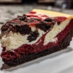 Close-up of a decadent slice of red velvet cheesecake showing distinct red, white, and dark chocolate layers.
