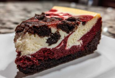 Close-up of a decadent slice of red velvet cheesecake showing distinct red, white, and dark chocolate layers.