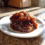 A glistening, dark mound of homemade apple butter served on a small white plate.