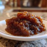 Close-up of a thick, dark brown scoop of homemade apple butter served on a small white dish.