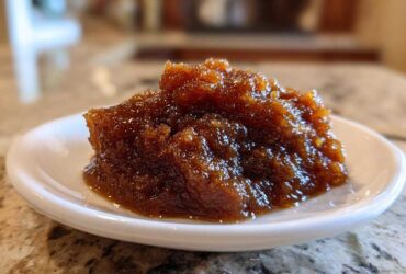 Close-up of a thick, dark brown scoop of homemade apple butter served on a small white dish.
