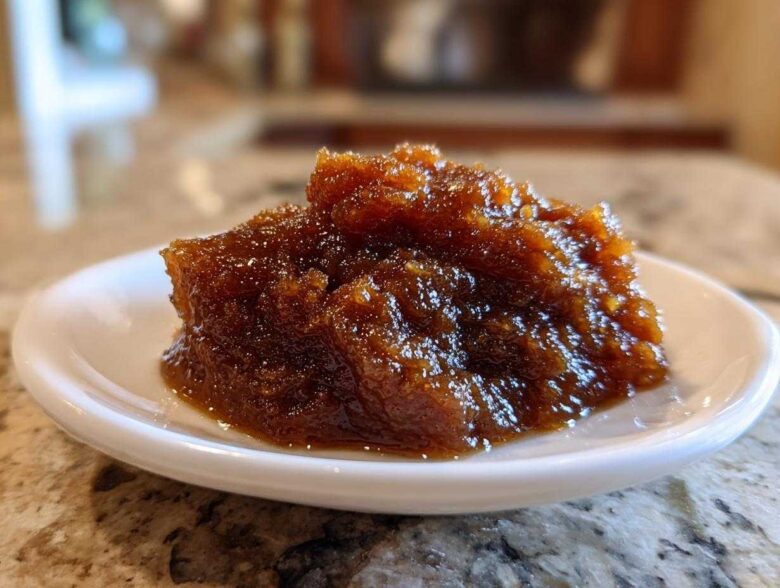 Close-up of a thick, dark brown scoop of homemade apple butter served on a small white dish.