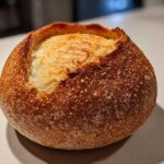 A single, round, crusty loaf ready to be turned into one of our amazing bread bowls, featuring a golden-brown exterior.