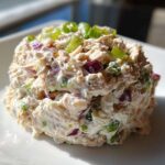 A perfectly scooped portion of healthy tuna salad mixed with creamy dressing, red onion, and green onions on a white plate.