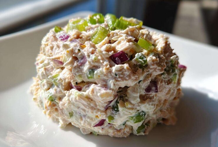 A perfectly scooped portion of healthy tuna salad mixed with creamy dressing, red onion, and green onions on a white plate.