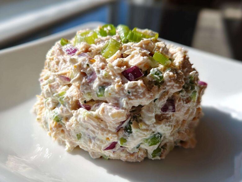 A perfectly scooped portion of healthy tuna salad mixed with creamy dressing, red onion, and green onions on a white plate.