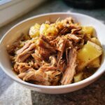 Close-up of tender, shredded pork and cooked sauerkraut served in a white bowl.