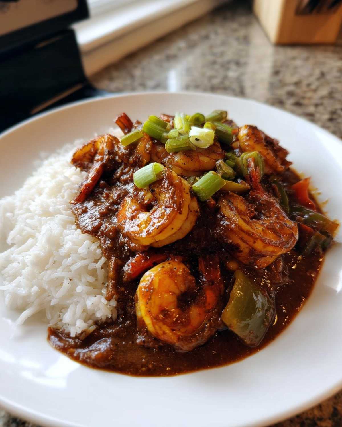 A close-up of a serving of rich, dark shrimp etouffee spooned over fluffy white rice, garnished with green onions.