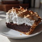 A perfect slice of chocolate meringue pie featuring a rich dark filling and towering, toasted meringue peaks.