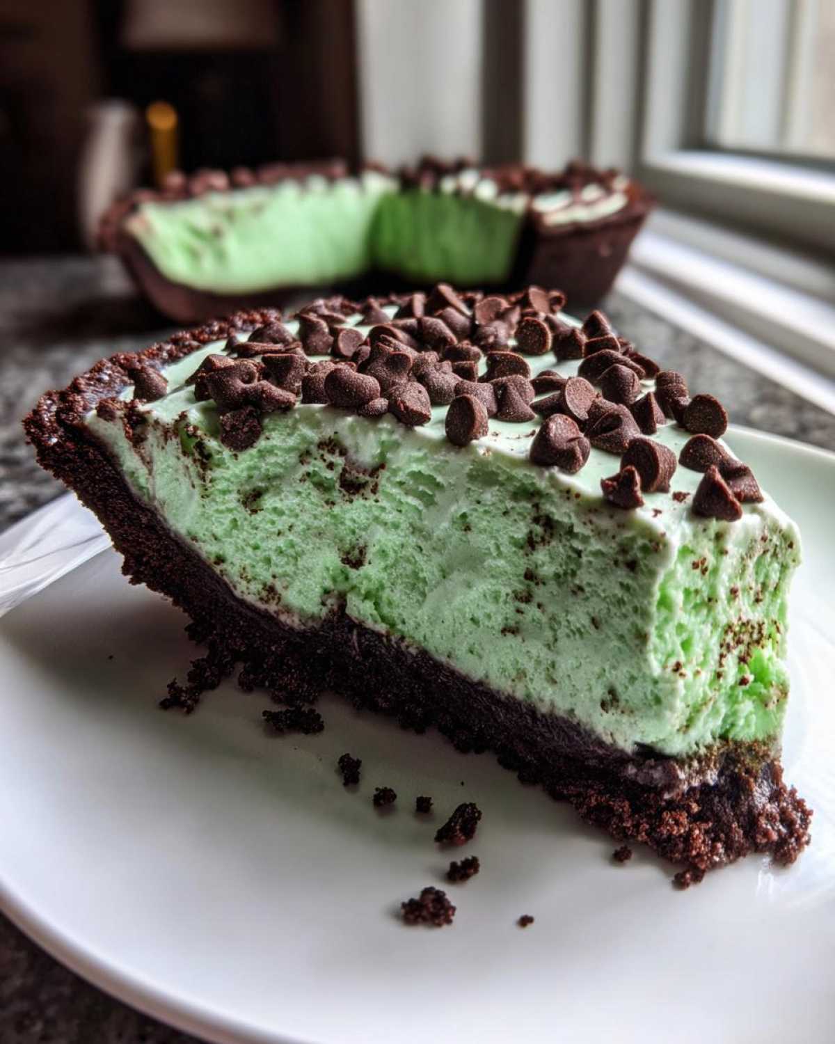 A close-up slice of bright green grasshopper pie with a dark chocolate crust, topped with mini chocolate chips.