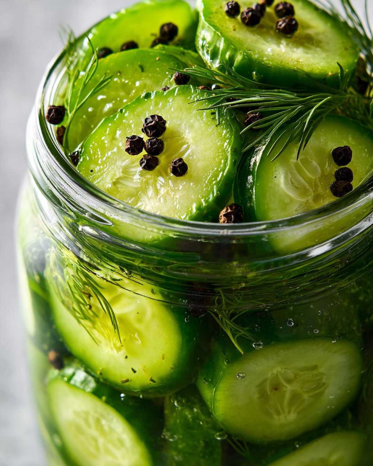 Close-up of bright green cucumber slices packed tightly in a jar for refrigerator pickles, seasoned with dill and black peppercorns.