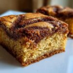 A close-up, mouthwatering shot of a single square of snickerdoodle blondies with a thick cinnamon swirl topping.