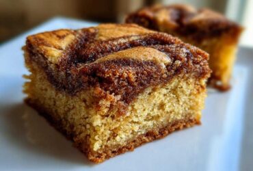 A close-up, mouthwatering shot of a single square of snickerdoodle blondies with a thick cinnamon swirl topping.