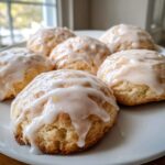 Close-up of soft ricotta cookies topped with a thick, dripping lemon glaze, sitting on a white plate.