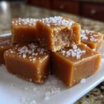 Close-up of soft, square salted caramels sprinkled with flaky sea salt on a white plate.