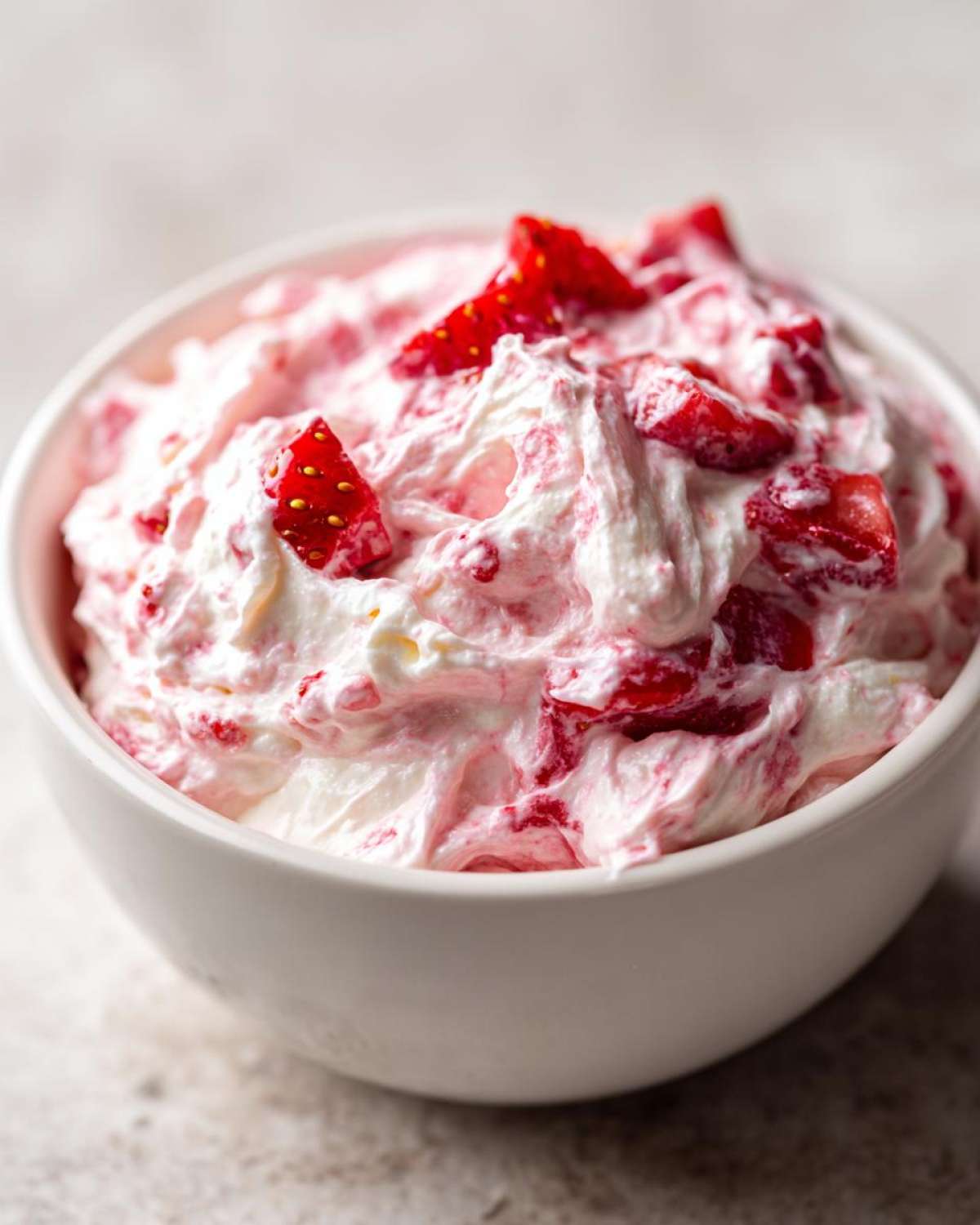 Close-up of fluffy strawberry cheesecake dip mixed with chunks of fresh strawberries in a white bowl.