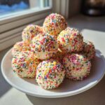 A pile of homemade sugar cookie truffles coated completely in rainbow nonpareils sprinkles.