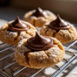 Close-up of freshly baked, sugar-coated kiss cookies topped with a melted chocolate kiss.
