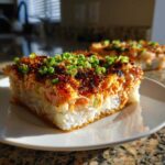A thick slice of baked sushi topped with crispy brown topping and fresh green onions on a white plate.