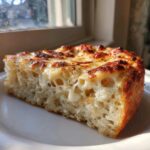 Close-up of a thick, airy slice of keto pizza crust topped with bubbly, browned mozzarella cheese.