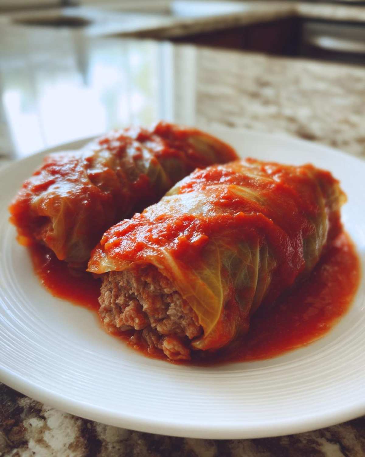 Close-up of two savory cabbage rolls stuffed with meat and covered in rich tomato sauce.