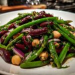 Close-up of a vibrant bean salad featuring green beans, dark red kidney beans, chickpeas, and red onion.