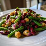 Close-up of a vibrant bean salad featuring green beans, kidney beans, chickpeas, and red onion on a white plate.