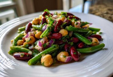 Close-up of a vibrant bean salad featuring green beans, kidney beans, chickpeas, and red onion on a white plate.